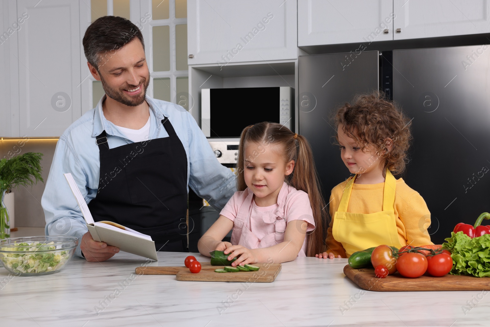 Photo of Happy man with his daughters cooking by recipe book in kitchen