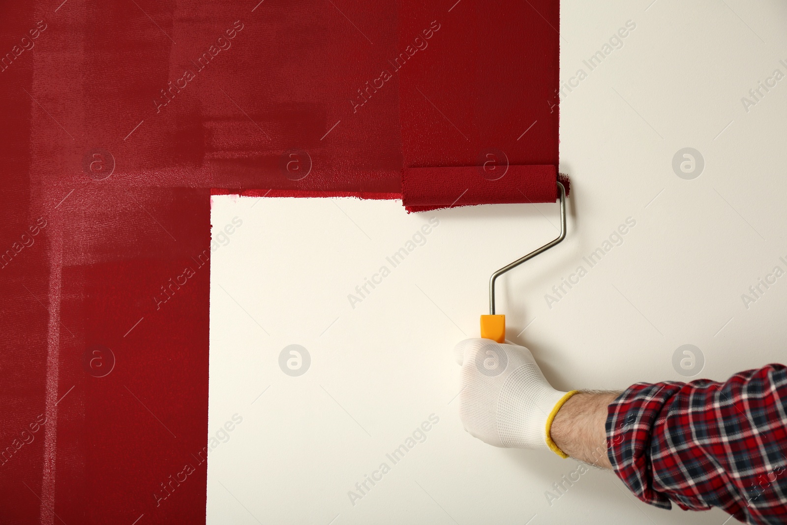 Photo of Man applying red paint with roller brush on white wall, closeup