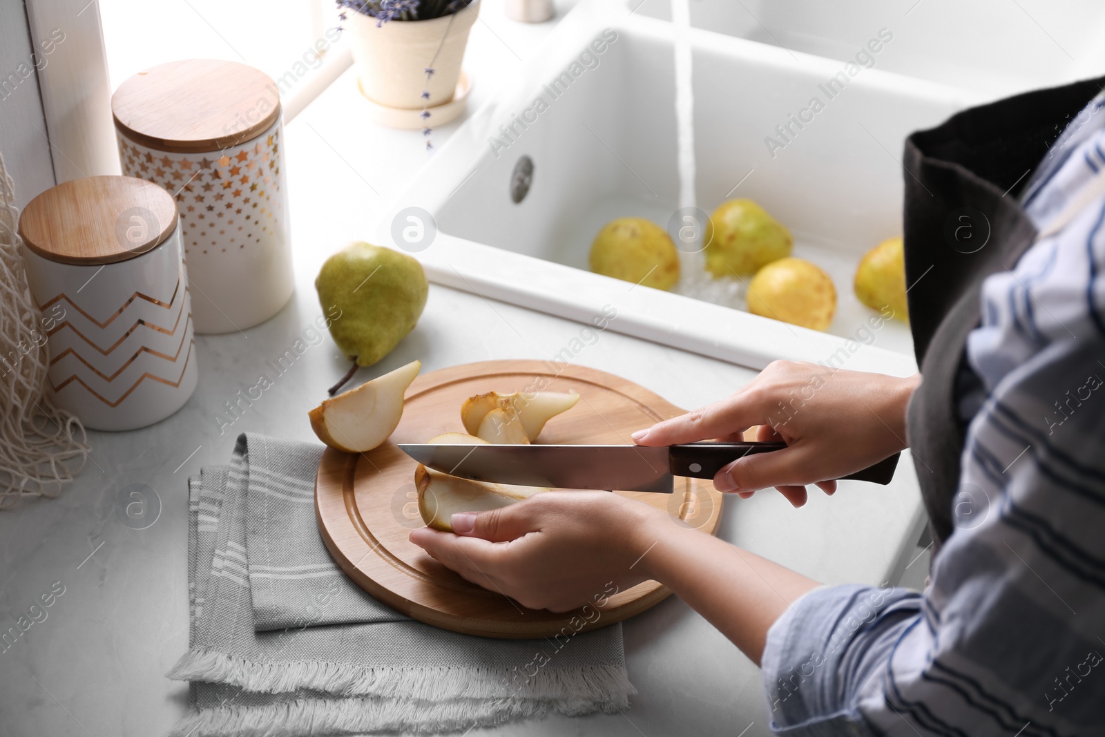 Photo of Woman cutting fresh ripe pear at table in kitchen, closeup