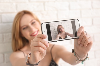 Attractive young woman taking selfie near brick wall, closeup