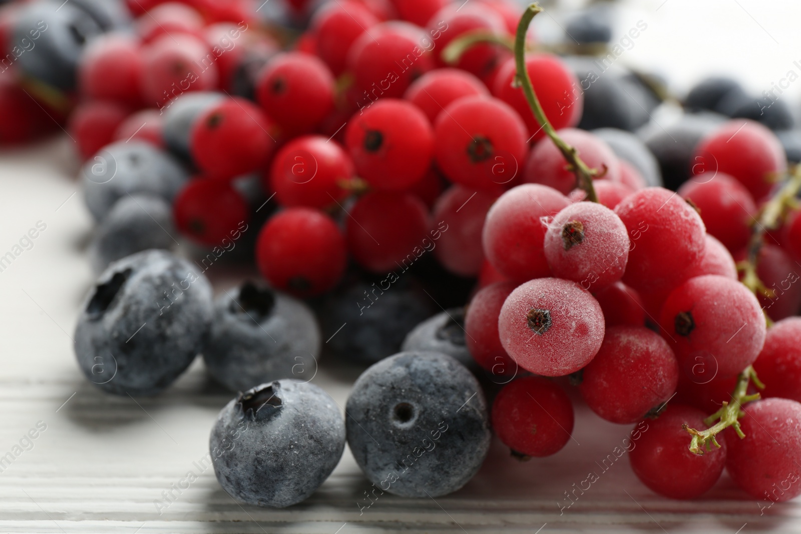 Photo of Tasty frozen blueberries and red currants on white wooden table, closeup