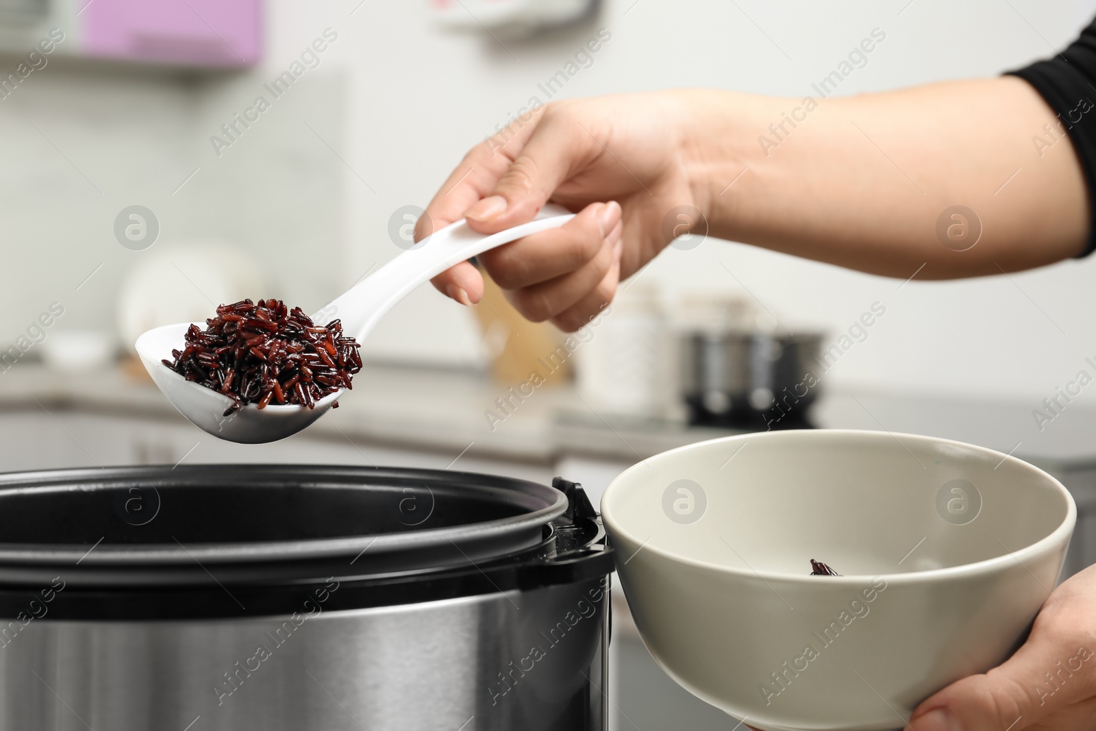 Photo of Woman putting brown rice into bowl from multi cooker in kitchen, closeup