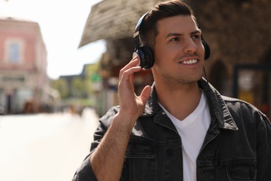 Photo of Handsome man with headphones listening to music on city street, space for text