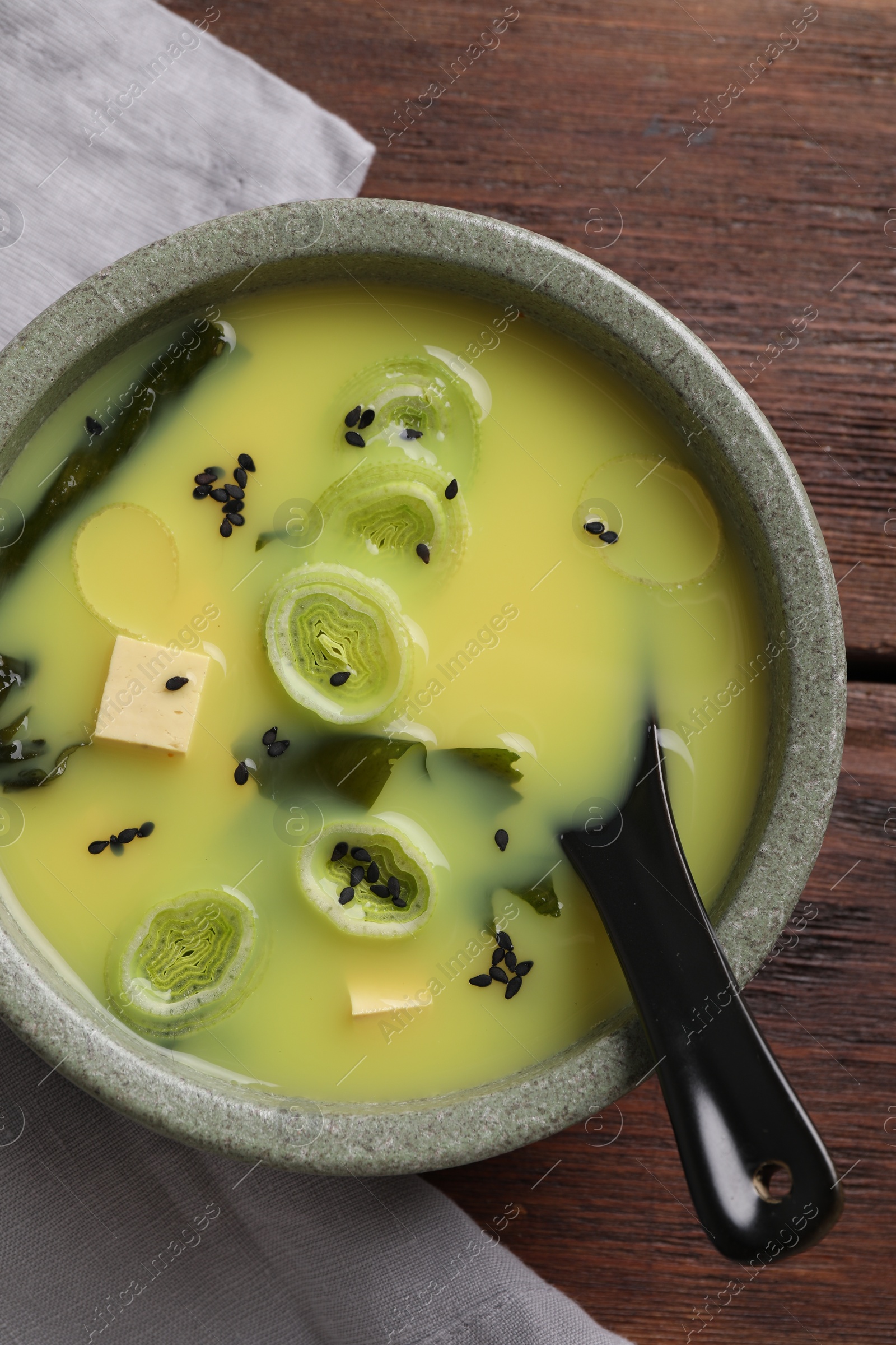 Photo of Bowl of delicious miso soup with tofu and spoon on wooden table, top view