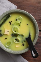 Bowl of delicious miso soup with tofu and spoon on wooden table, top view