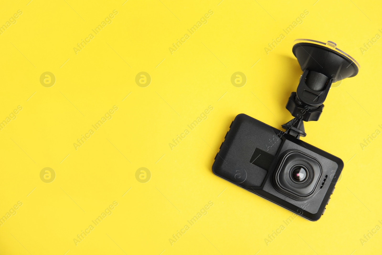 Photo of Modern car dashboard camera with suction mount on yellow background, top view. Space for text