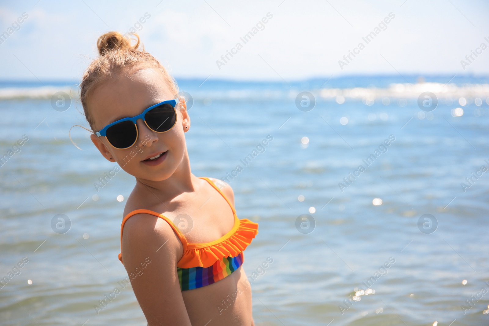 Photo of Little girl with stylish sunglasses in sea on sunny day, space for text. Beach holiday