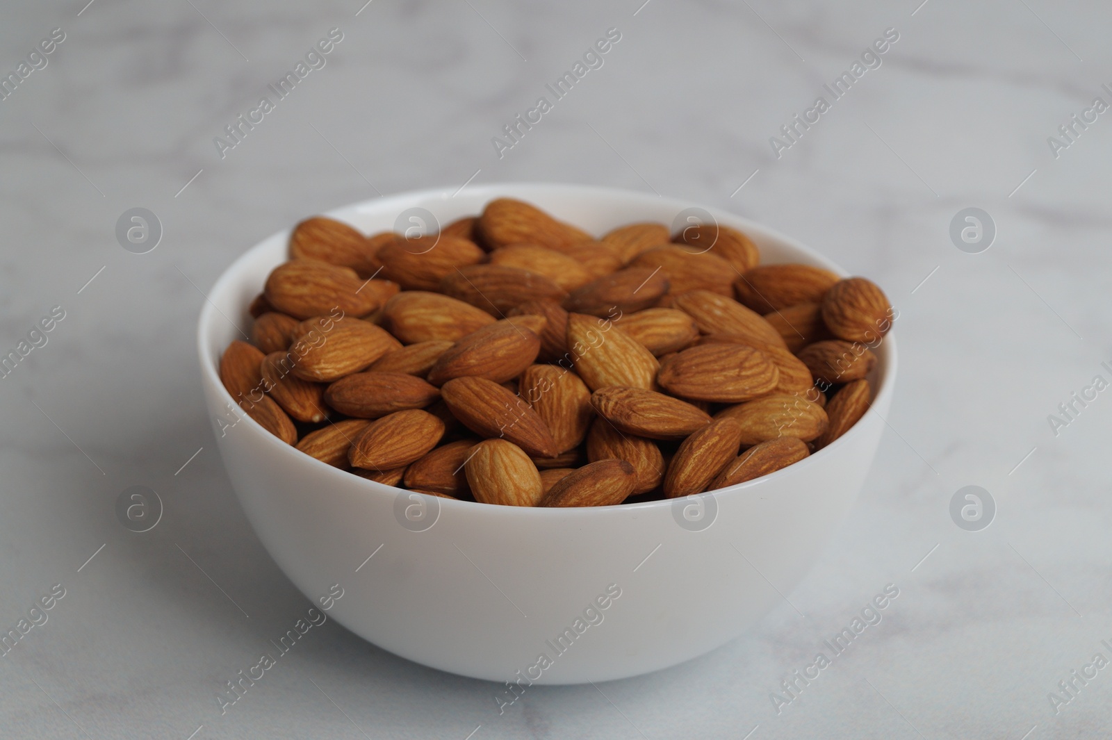 Photo of Bowl of delicious almonds on white marble table