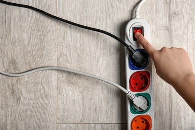 Woman pressing power button of extension cord on wooden floor, top view with space for text. Electrician's equipment