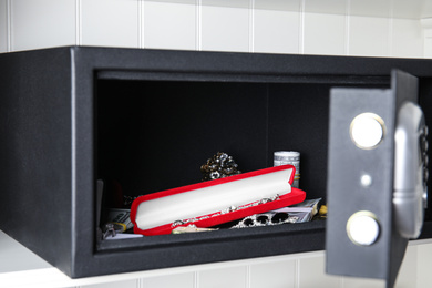 Photo of Open black steel safe with money and jewelry on shelf