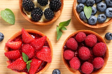 Tartlets with different fresh berries on wooden table, flat lay. Delicious dessert