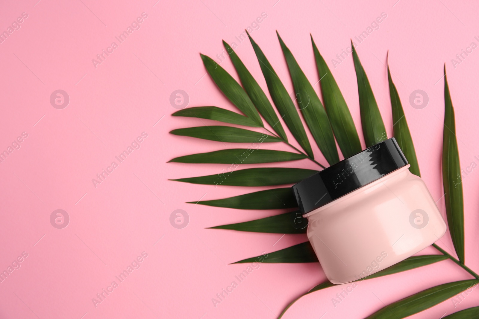 Photo of Jar of cream and palm leaf on pink background, top view. Space for text