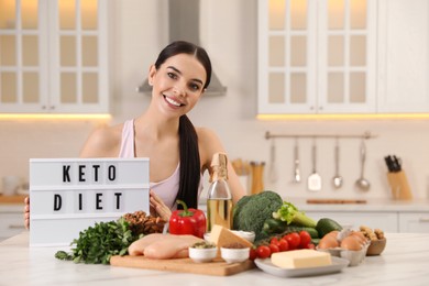 Photo of Happy woman near lightbox with words Keto Diet and different products in kitchen