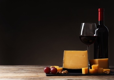 Photo of Delicious cheese served with red wine on table against dark background. Space for text