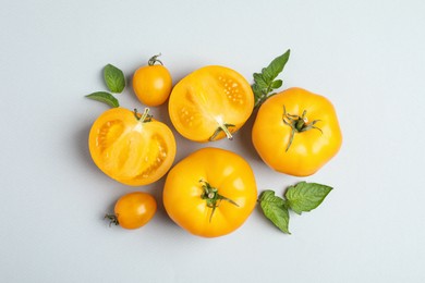 Cut and whole ripe yellow tomatoes with leaves on light background, flat lay