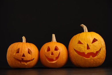 Spooky Jack pumpkin head lanterns on grey table against black background, space for text. Halloween decoration