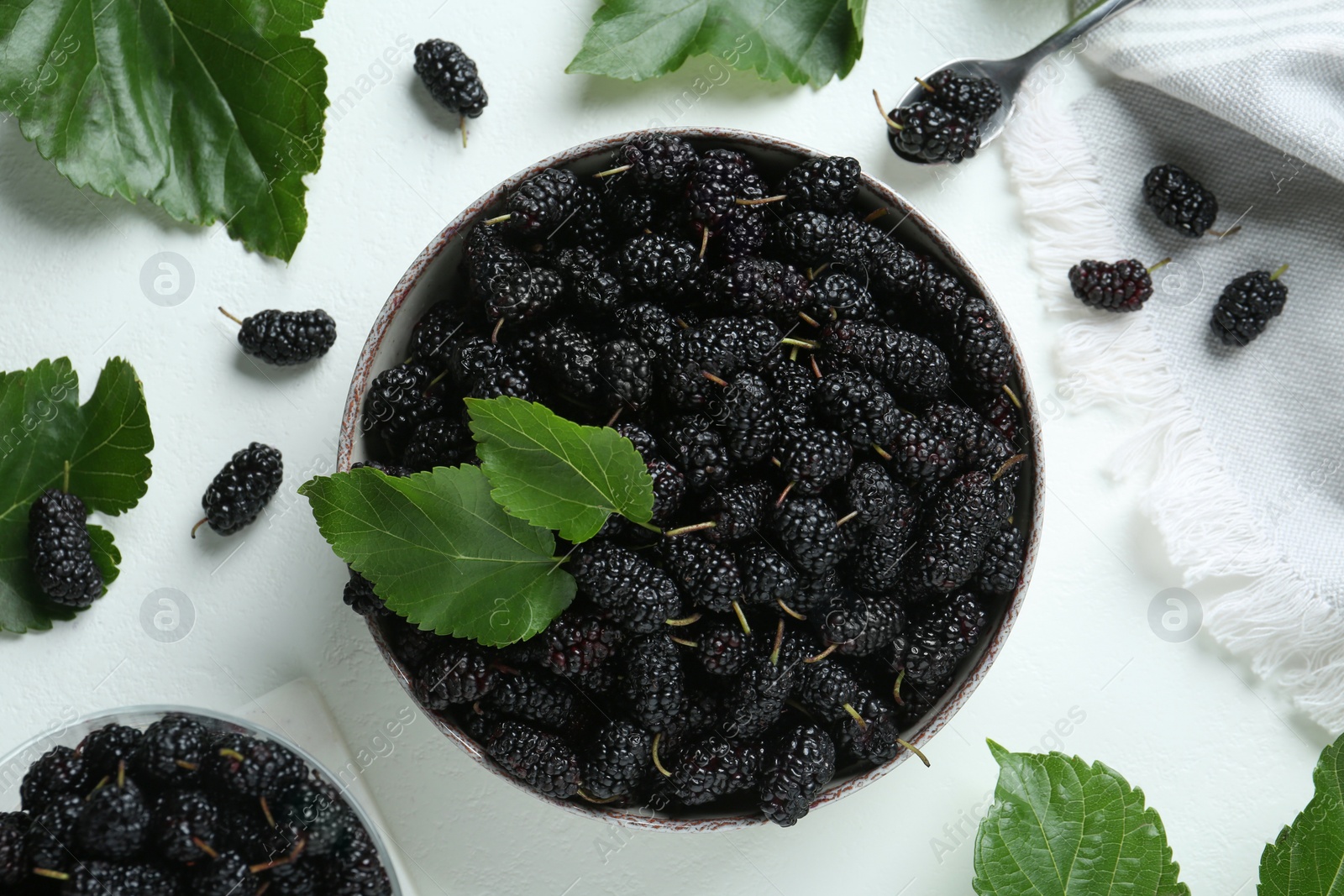 Photo of Bowl of delicious ripe black mulberries on white table, flat lay