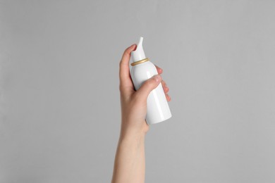 Woman holding nasal spray on grey background, closeup