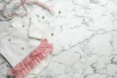 Photo of Cute knitted baby bodysuit on white marble background, top view. Space for text