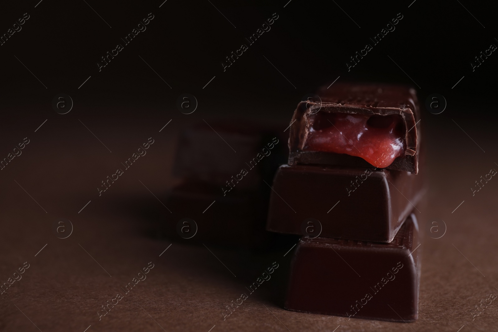 Photo of Tasty dark chocolate candies with liquid filling on brown table, closeup. Space for text