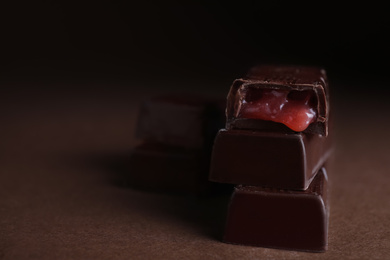 Tasty dark chocolate candies with liquid filling on brown table, closeup. Space for text