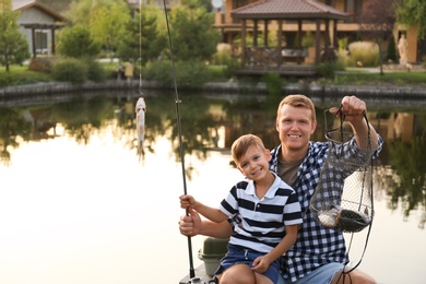 Photo of Dad and son fishing together on sunny day. Space for text