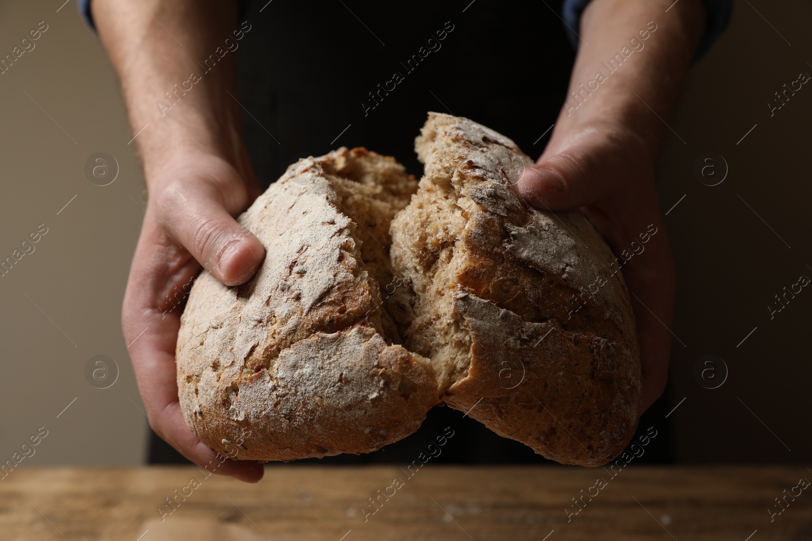 Photo of Man breaking loaf of fresh bread at wooden table, closeup