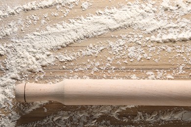 Photo of Scattered flour and rolling pin on wooden table, top view