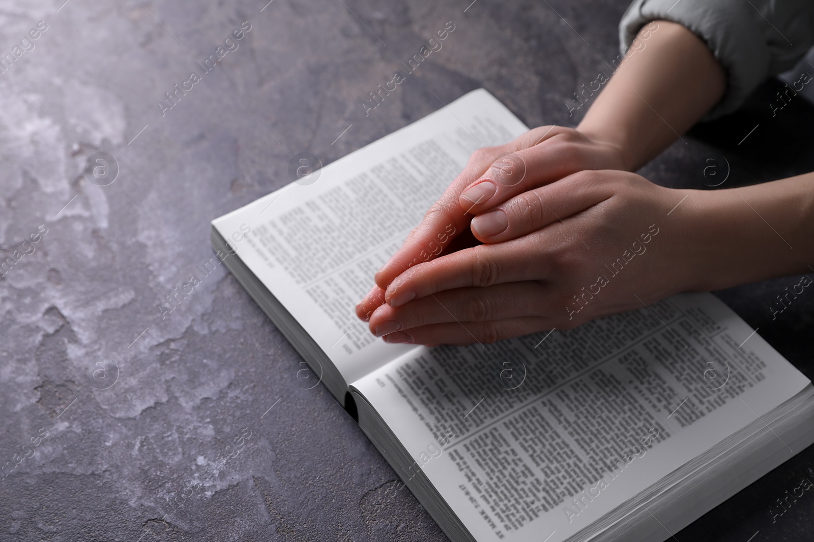 Photo of Religion. Christian woman praying over Bible at gray table, closeup