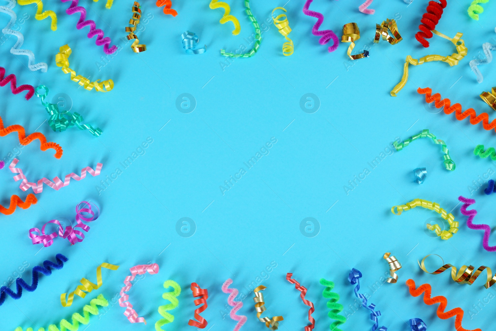 Photo of Frame of colorful serpentine streamers and fluffy wires on light blue background, flat lay. Space for text