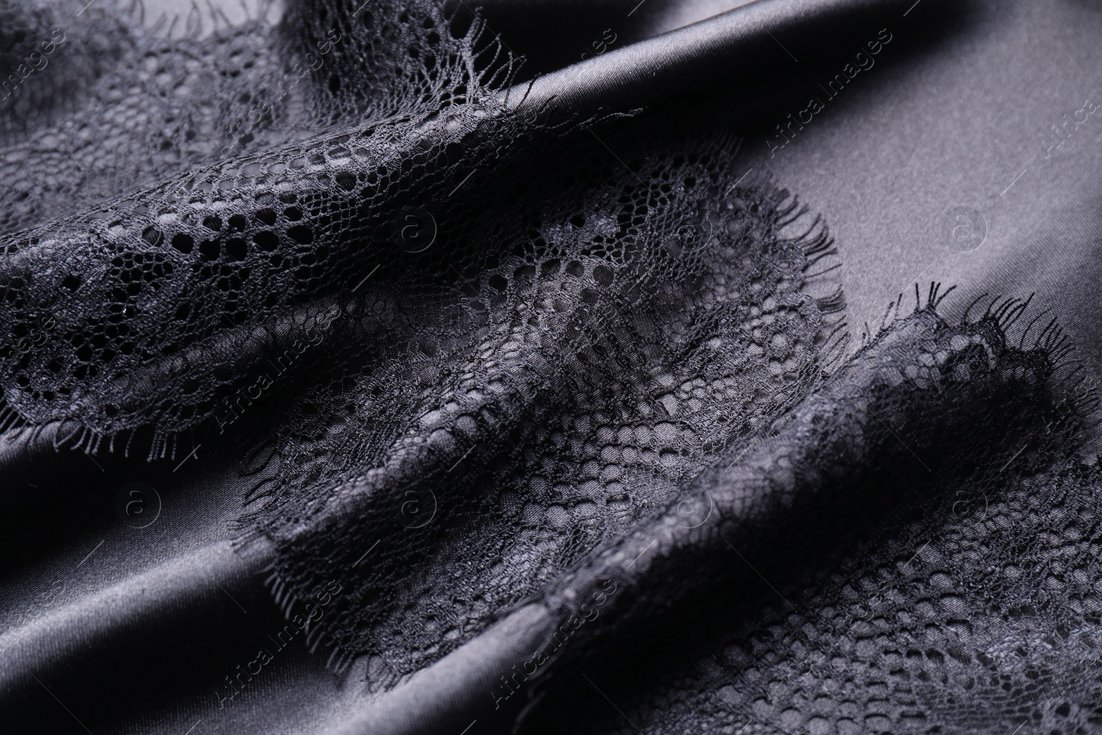 Photo of Beautiful lace with pattern on black fabric, closeup