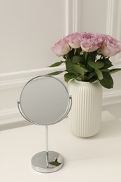 Mirror and vase with pink roses on white dressing table