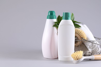 Photo of Bottles of cleaning product, brushes, rags and green leaves on light background. Space for text