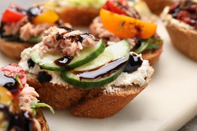 Photo of Delicious bruschettas with balsamic vinegar and different toppings on white board, closeup