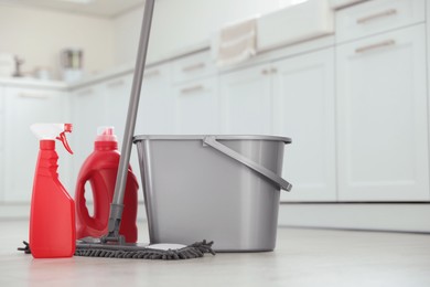 Photo of Mop, detergents and plastic bucket in kitchen. Cleaning supplies