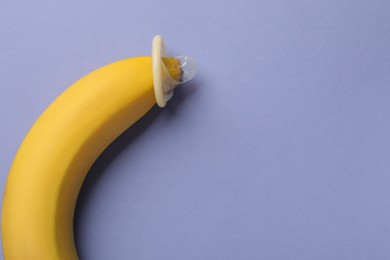 Photo of Banana with condom on violet background, top view and space for text. Safe sex concept