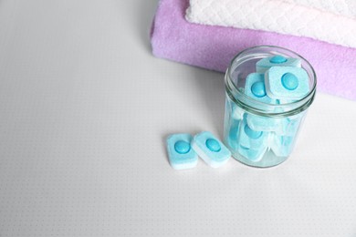 Photo of Jar with water softener tablets near stacked towels on table, space for text