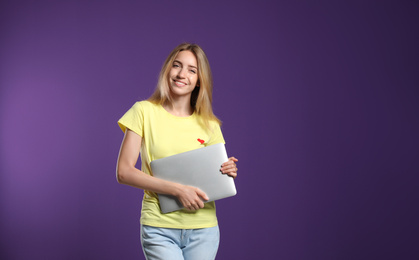Portrait of young woman with modern laptop on purple background