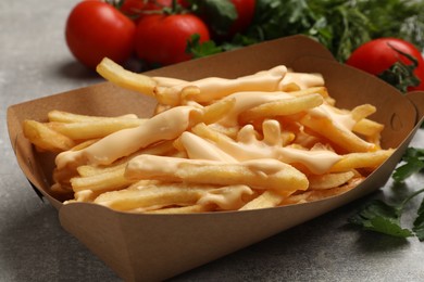 Photo of Tasty potato fries, cheese sauce in paper container and products on grey table, closeup