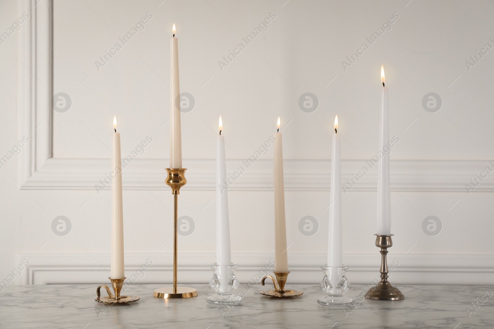 Photo of Elegant candlesticks with burning candles on white marble table