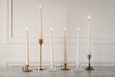 Photo of Elegant candlesticks with burning candles on white marble table