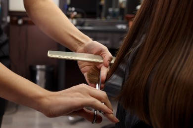 Photo of Professional hairdresser cutting woman's hair in salon, closeup