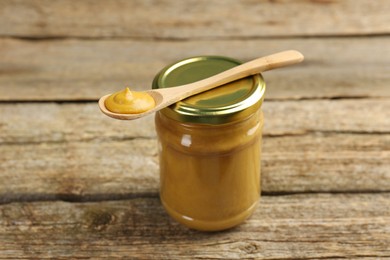 Photo of Jar and spoon with tasty mustard sauce on wooden table, closeup