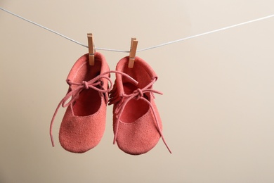 Photo of Cute small shoes hanging on washing line against color background, space for text. Baby accessories