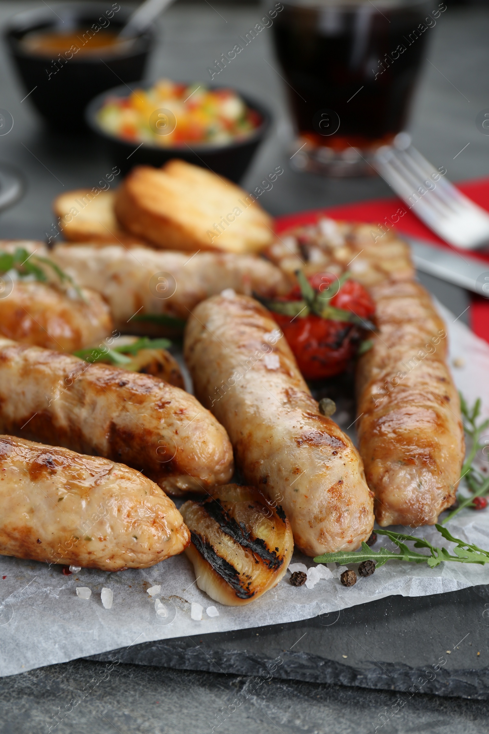 Photo of Tasty fresh grilled sausages with vegetables on grey table, closeup