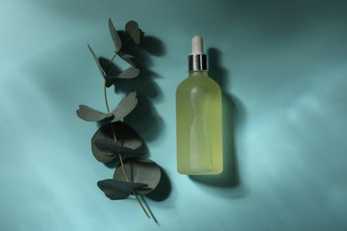 Photo of Bottle of hydrophilic oil and eucalyptus branch on light blue background, flat lay