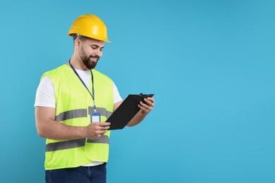 Photo of Engineer in hard hat holding clipboard on light blue background, space for text