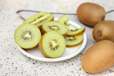 Photo of Whole and cut fresh kiwis on white table with pattern, closeup