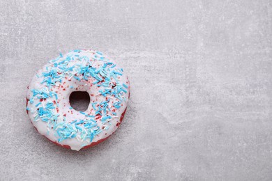 Sweet glazed donut decorated with sprinkles on light grey table, top view and space for text. Tasty confectionery