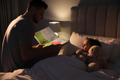 Photo of Father reading bedtime story to his daughter at home